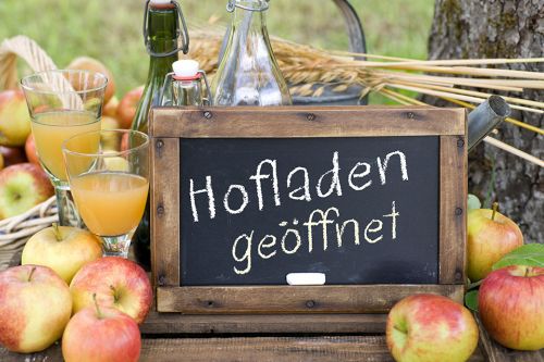 Tafel mit Aufschrift Hofladen geöffnet, daneben Äpfel und Saft